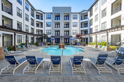 an outdoor pool with blue chairs and umbrellas in front of an apartment building